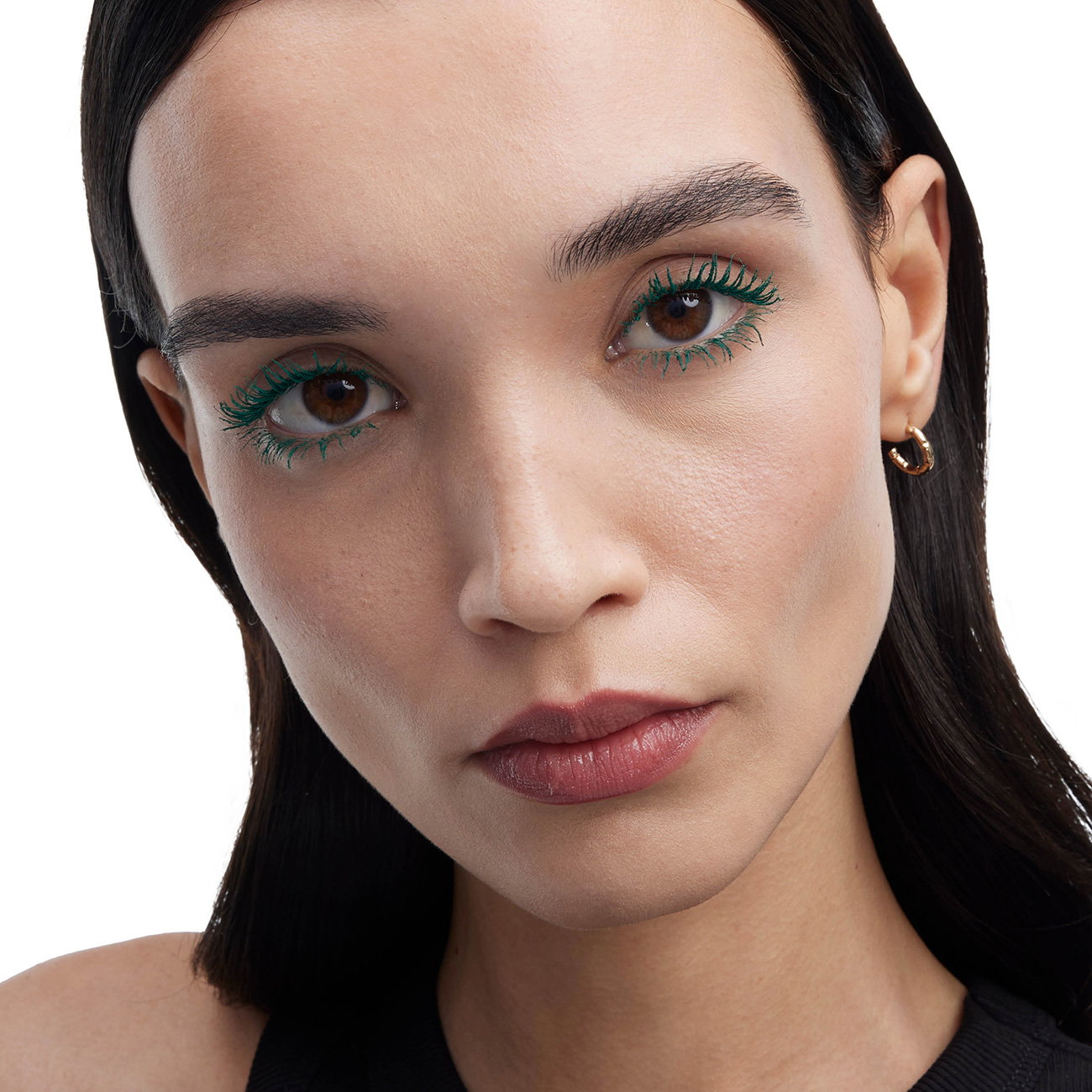A close-up portrait of a woman showcasing vibrant green mascara on her eyelashes.