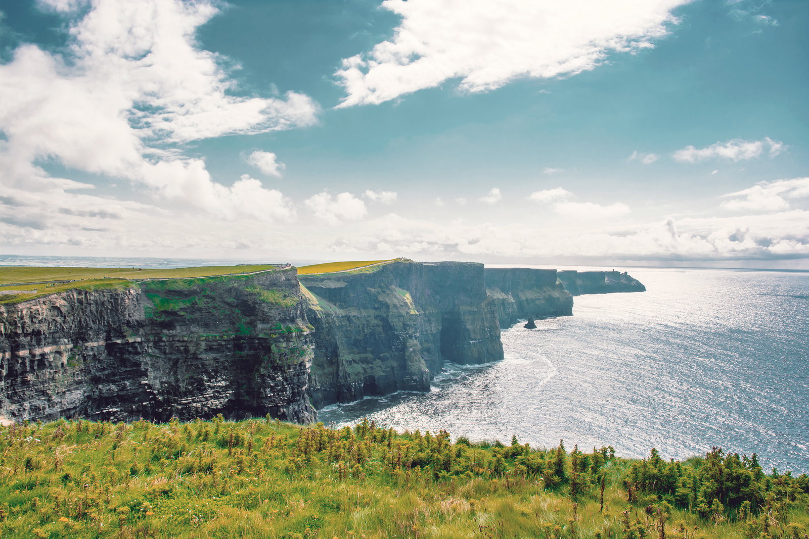 Los Acantilados de Moher extendiéndose hacia el horizonte bajo un cielo de nubes blancas, con el Atlántico al fondo