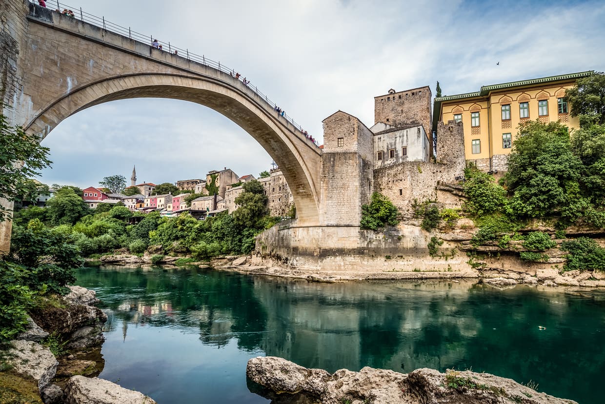 El Stari Most de Mostar visto desde la orilla del Neretva turquesa, con viajeros cruzando el puente