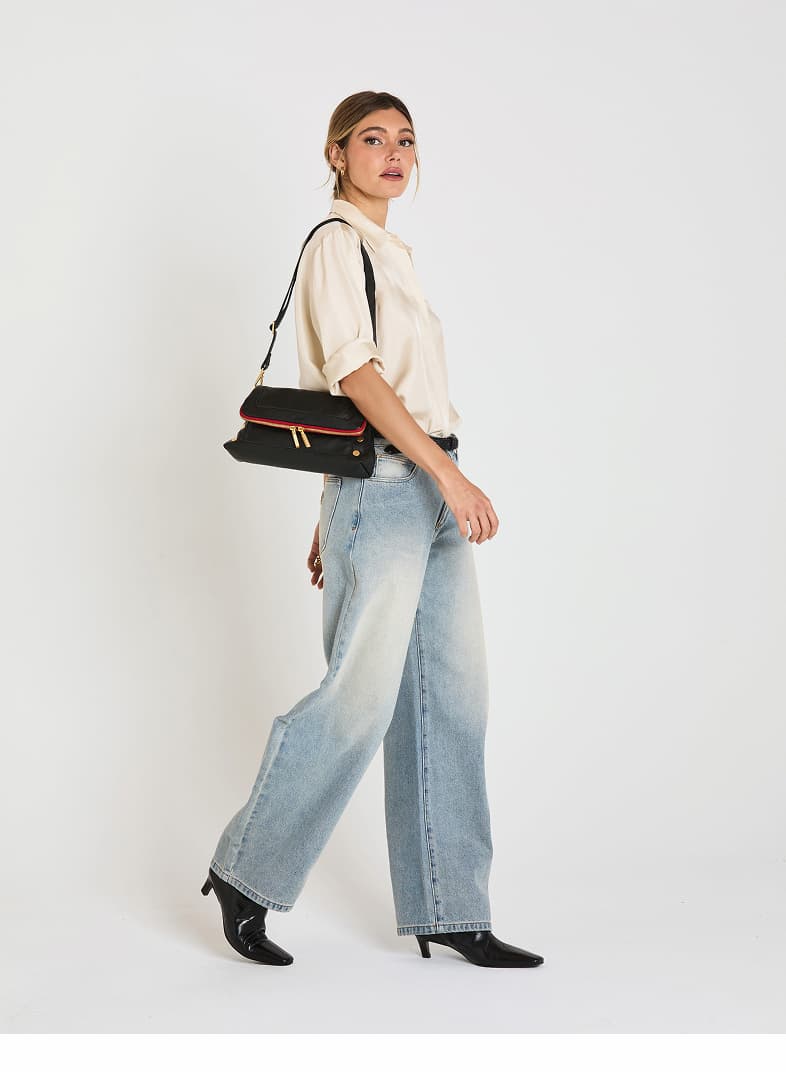 Model wearing the Hammitt Beverly Med in Black/Brushed Gold Red Zip as a shoulder bag, showcasing the structured silhouette, signature rivets, brushed gold hardware, and red zipper.