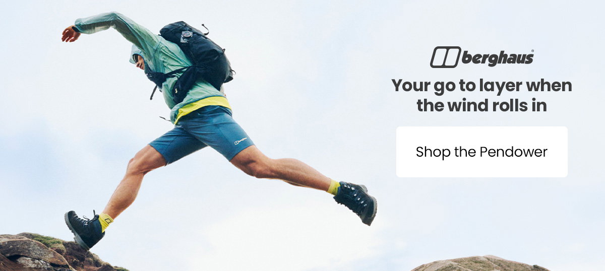 Person wearing a Berghaus lightweight jacket and backpack jumps between rocks outdoors, with the text “Your go to layer when the wind rolls in” and a “Shop the Pendower” call-to-action.