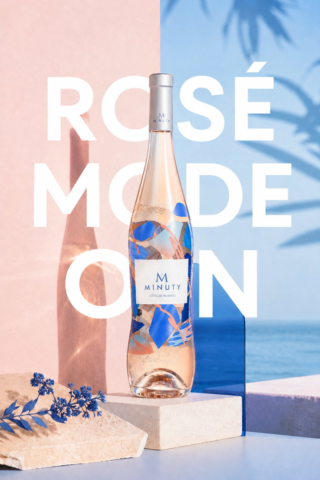 Bottle of Minuty rosé wine on pink and blue split background with bold 'ROSÉ MODE ON' text, coastal shadow and floral props