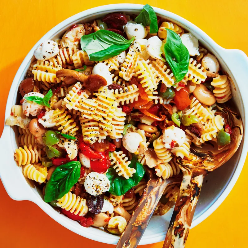 Radiatore, oil-packed sun dried tomatoes, chopped mixed olives, roasted red peppers, marinated artichokes, mixed pitted olives, marinated white beans, marinated mushrooms, and Ciliegine tossed in a bowl in a red wine vinaigrette and topped with fresh basil leaves.