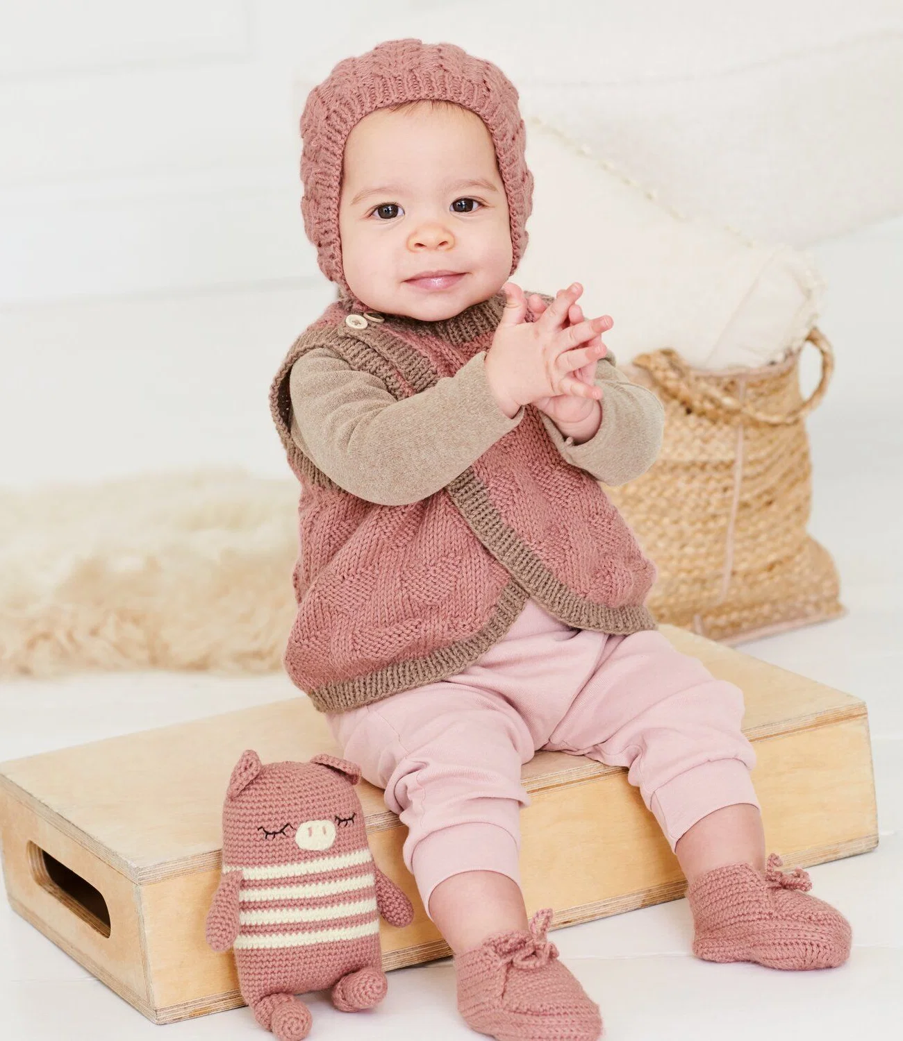 Baby mit Strickmütze, Strickweste und gehäkelten Schühchen
