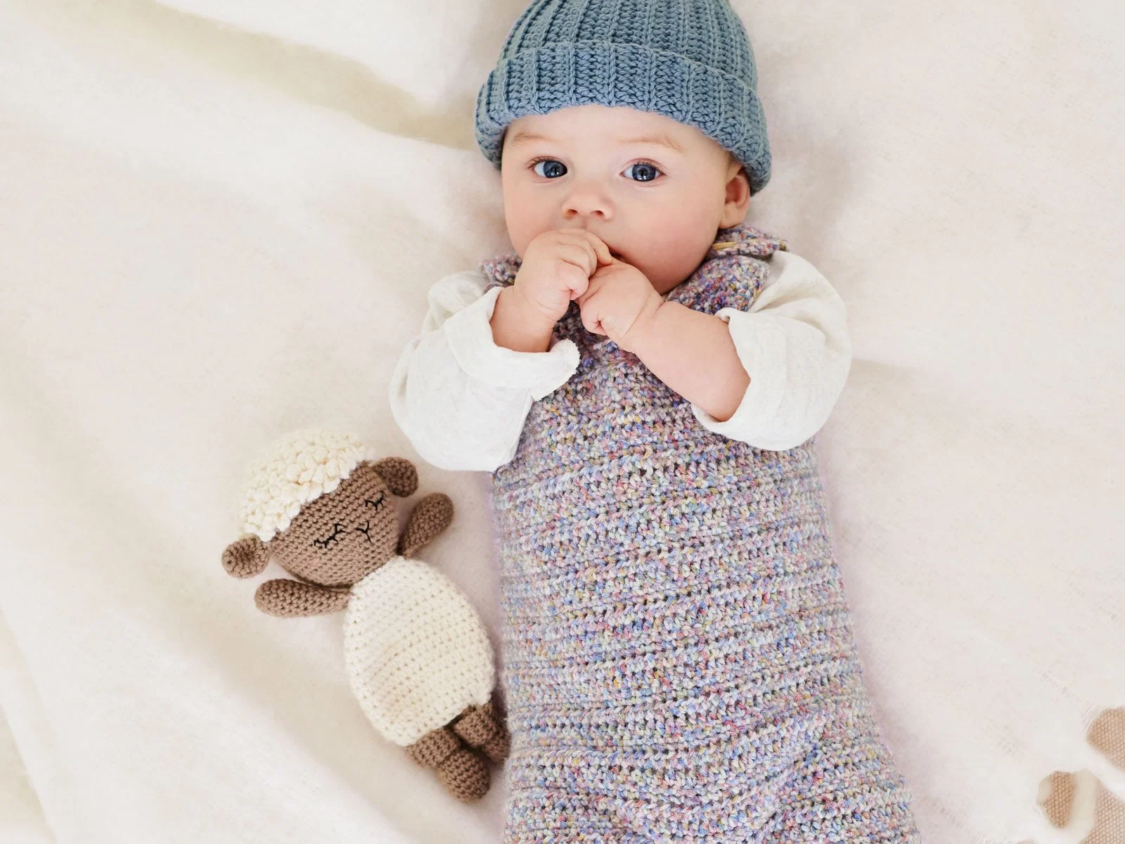 Baby mit blauer Mütze, Strampler und Schäfchenpuppe aus dem Anleitungsheft Rico Baby 044