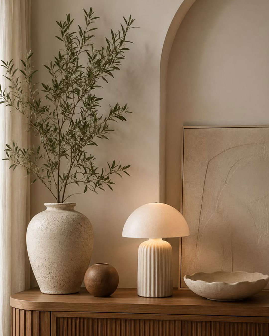 Neutral interior: wooden console with illuminated mushroom-style ceramic lamp, large textured vase with olive branches, small pottery and scalloped bowl