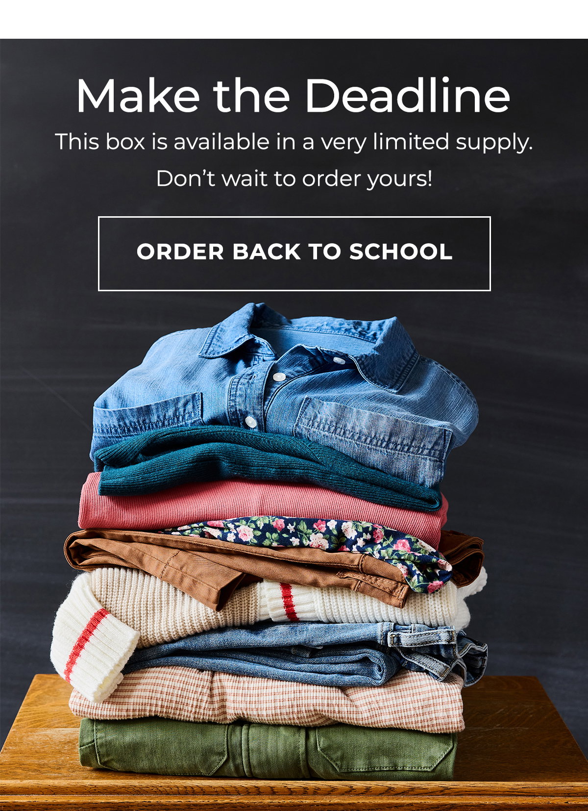 Folded back to school outfits stacked on a wooden desk against a chalkboard.