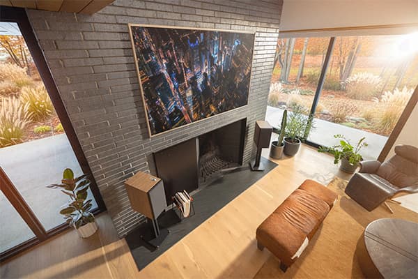 The Nines II Powered Speakers on stands, on either side of a gray brick fireplace, in a modern, living room.