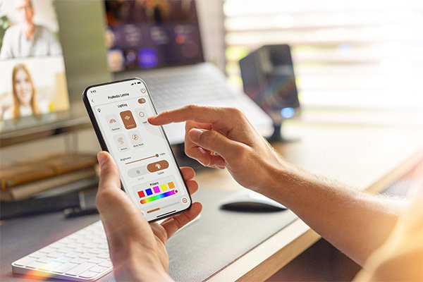 Image of someone using the Klipsch mobile app on their smartphone, with a modern desktop computer and speakers in the background.