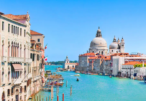 A scenic view of Venice's Grand Canal, featuring historic buildings and boats under a clear blue sky.