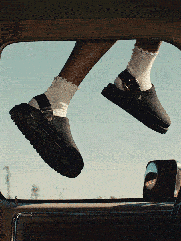 A GIF of a persons legs in a car window wearing UGG Clogs.