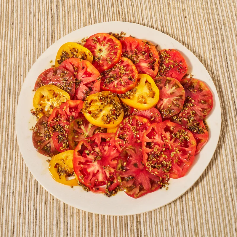 Brown Butter Tomatoes beautifully stacked on a white plate placed on a striped surface