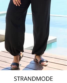 Model am Meer mit roten Strandtop und schwarzer Strandhose und link in die Strandmode