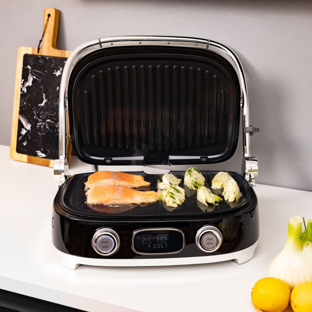 Grill Multiusos Smeg con placas grill acanaladas cocinando filetes de salmón y verduras sobre una encimera de cocina