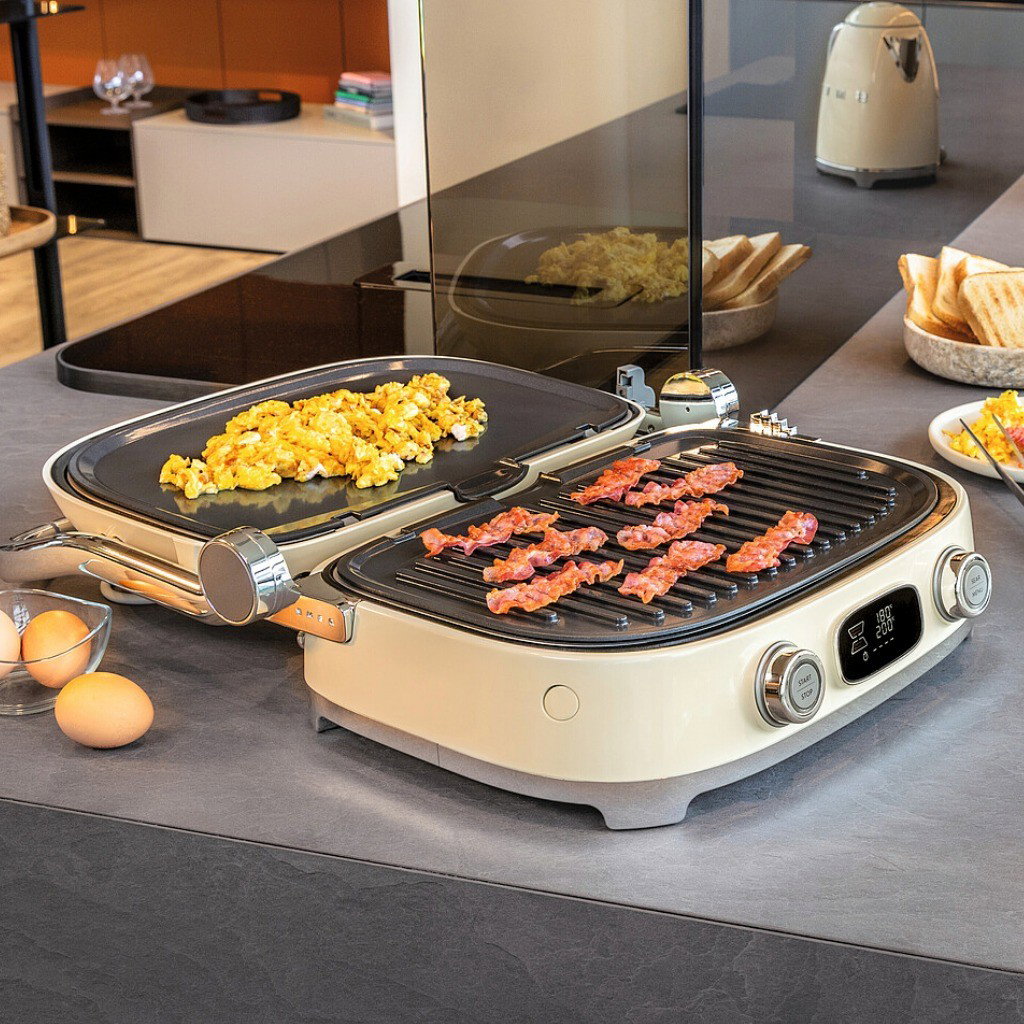 Grill Multiusos Smeg abierto en modo barbacoa, con placa grill y placa lisa para cocinar beicon y huevos revueltos
