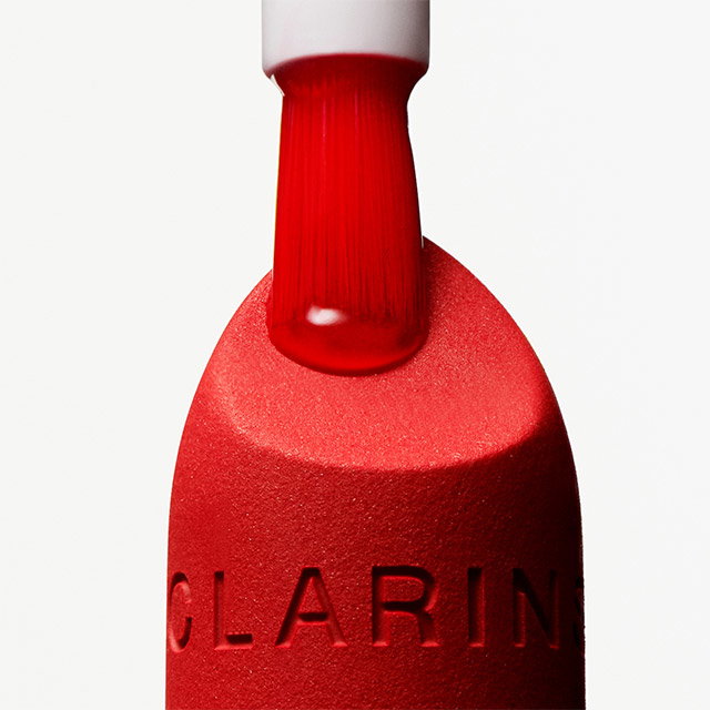 Bright red bottle with a matching cap featuring a dipper applicator, positioned upright against a plain background with 'CLARINS' embossed near the base.