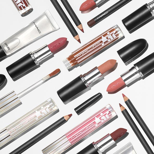 Various MAC lip products, including lipsticks in different shades of pink and brown, lip glosses, and lip liners arranged on a light background. Each item is displayed open with some caps placed beside them. The layout is neat, showcasing the brand name prominently.