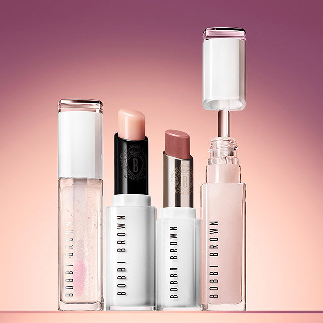 Bobbi Brown cosmetics featuring three lip products in nude shades and a clear container against a gradient pink background. Each item has a minimalist white and black design.