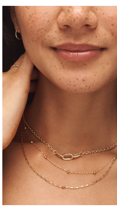 Woman wearing layered yellow gold necklaces, hoop earrings and ring.