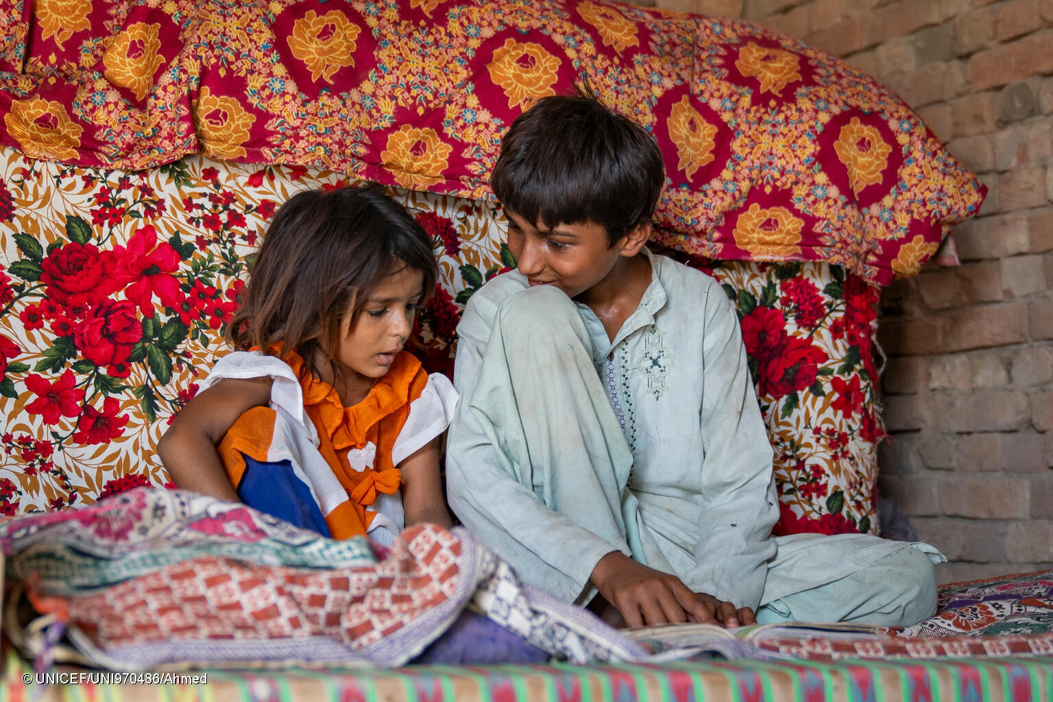 Wasim, 7, and his younger sister share a moment of friendship together as they read inside their home.