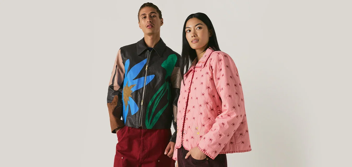 Deux jeunes adultes portant des vestes colorées se tiennent côte à côte devant un fond clair uni, regardant droit devant avec une expression neutre.