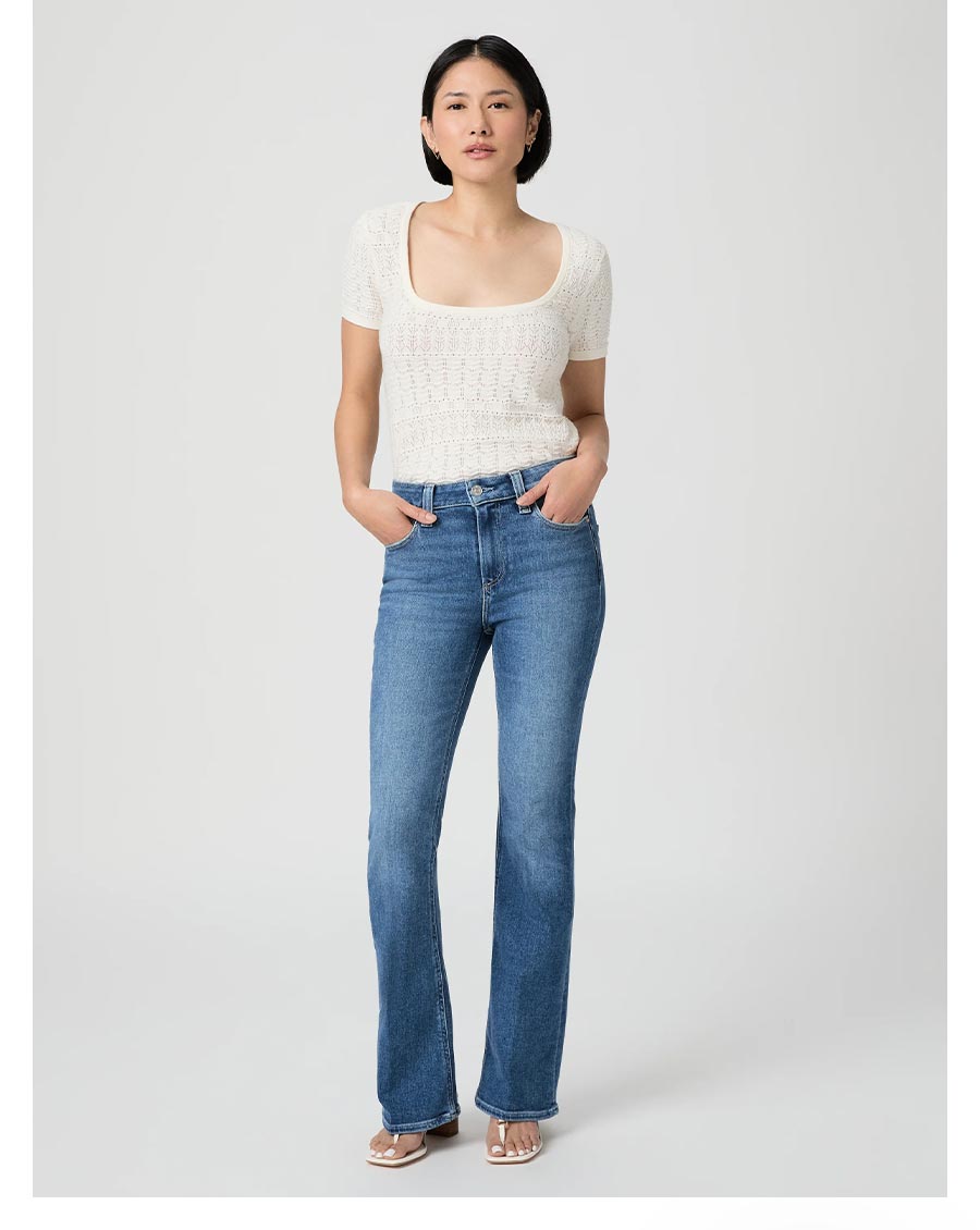 Woman wearing a pair of medium wash high rise flare jeans with a white knit short sleeve square neckline top