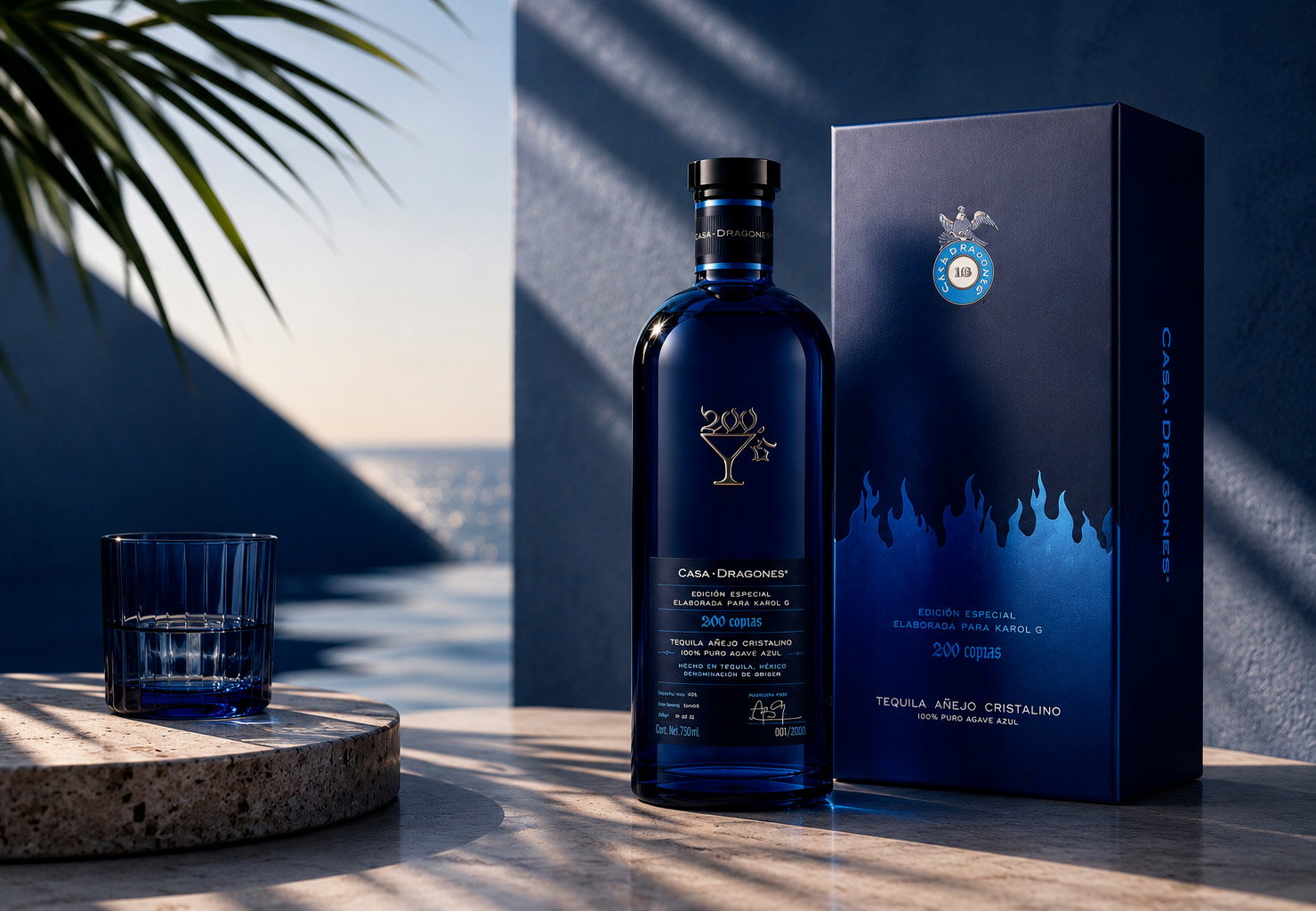 Luxury Casa Dragones blue tequila bottle and box with glass on sunlit terrace, sea view and palm shadows showcasing premium packaging