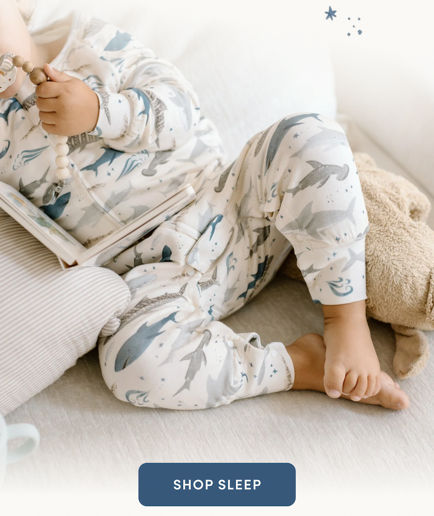 toddler wearing a shark printed sleep suit and reading a book