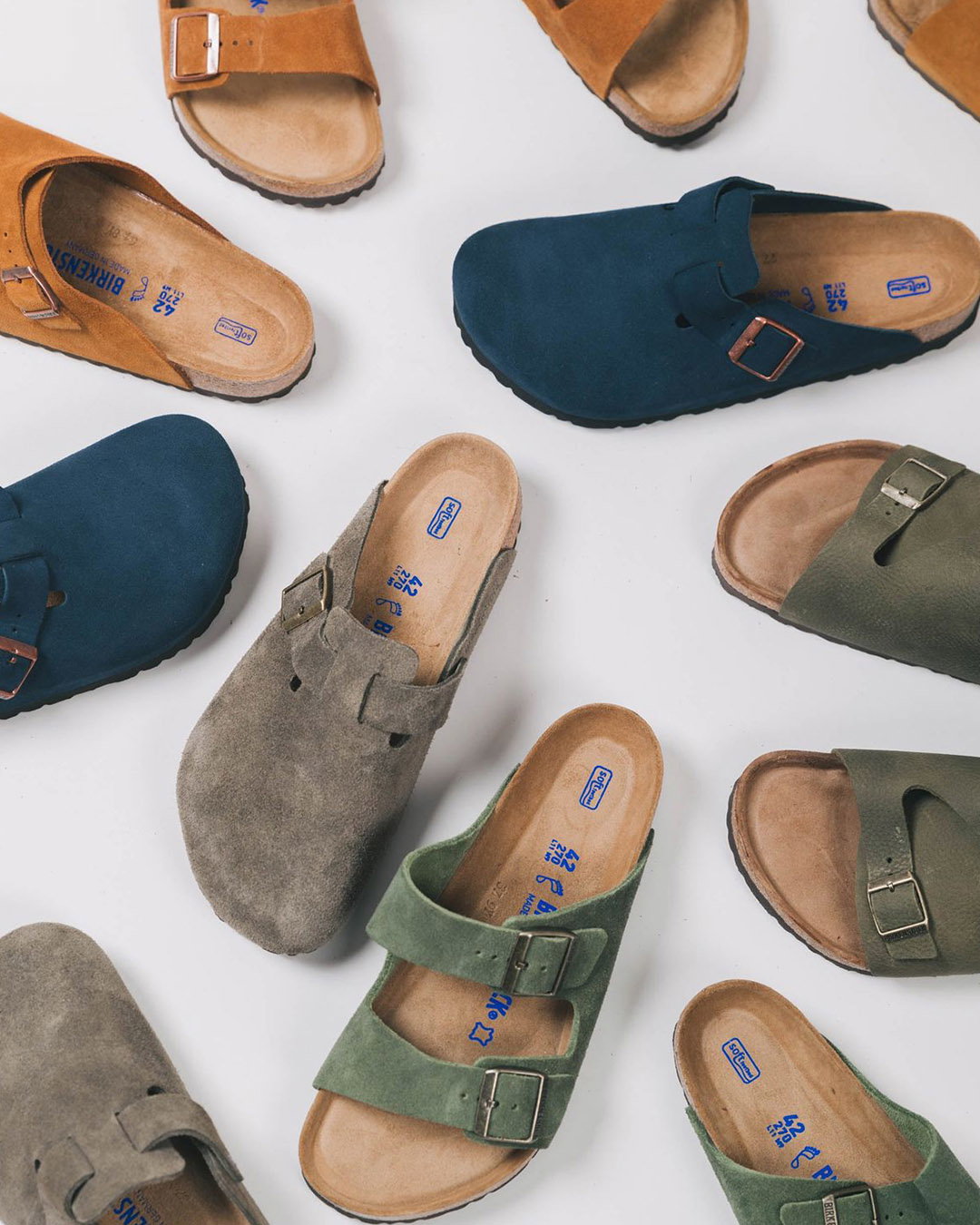Flat lay of suede buckle sandals in blue, green, grey and tan on a white background — women's casual slip-on cork-footbed shoes
