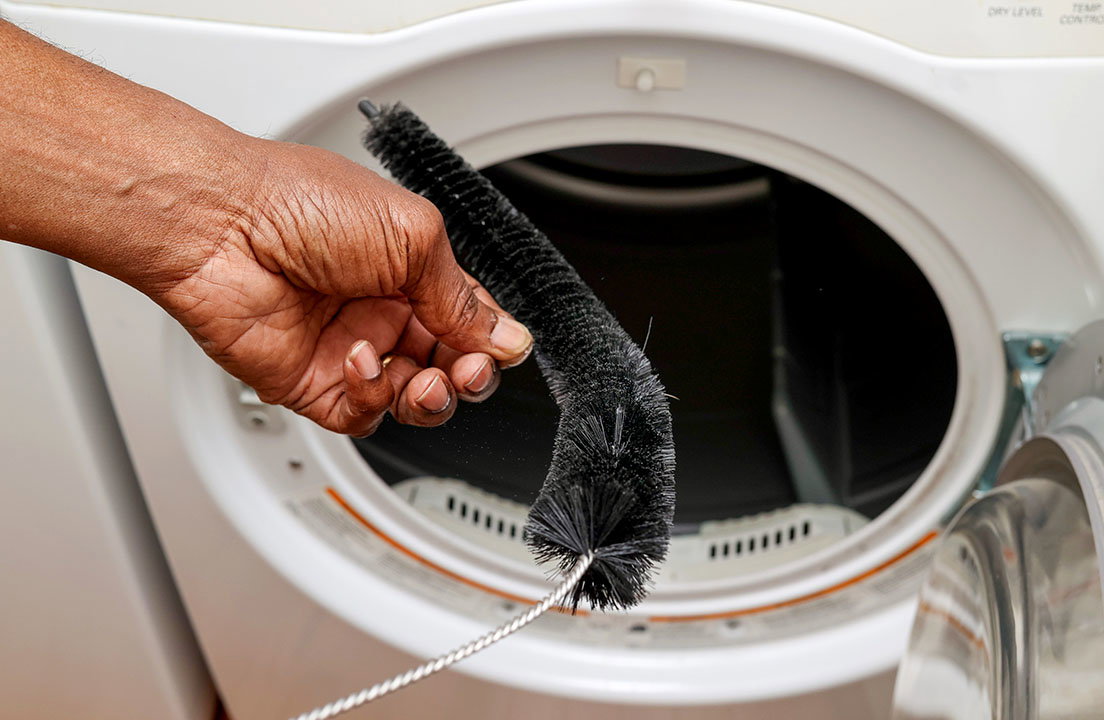 Hand holds a vent cleaning brush in front of an open dryer