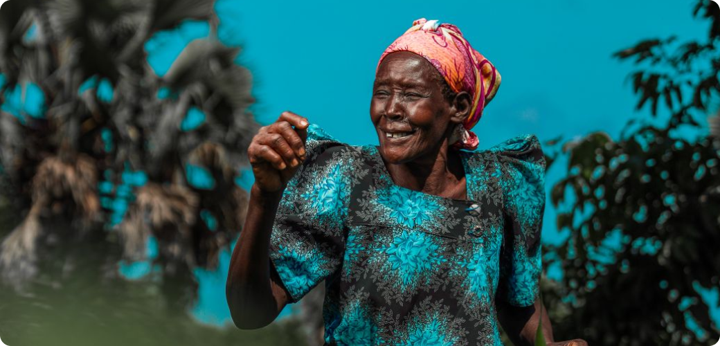 A woman laughing and smiling in a blue and black dress and a peach headscarf.