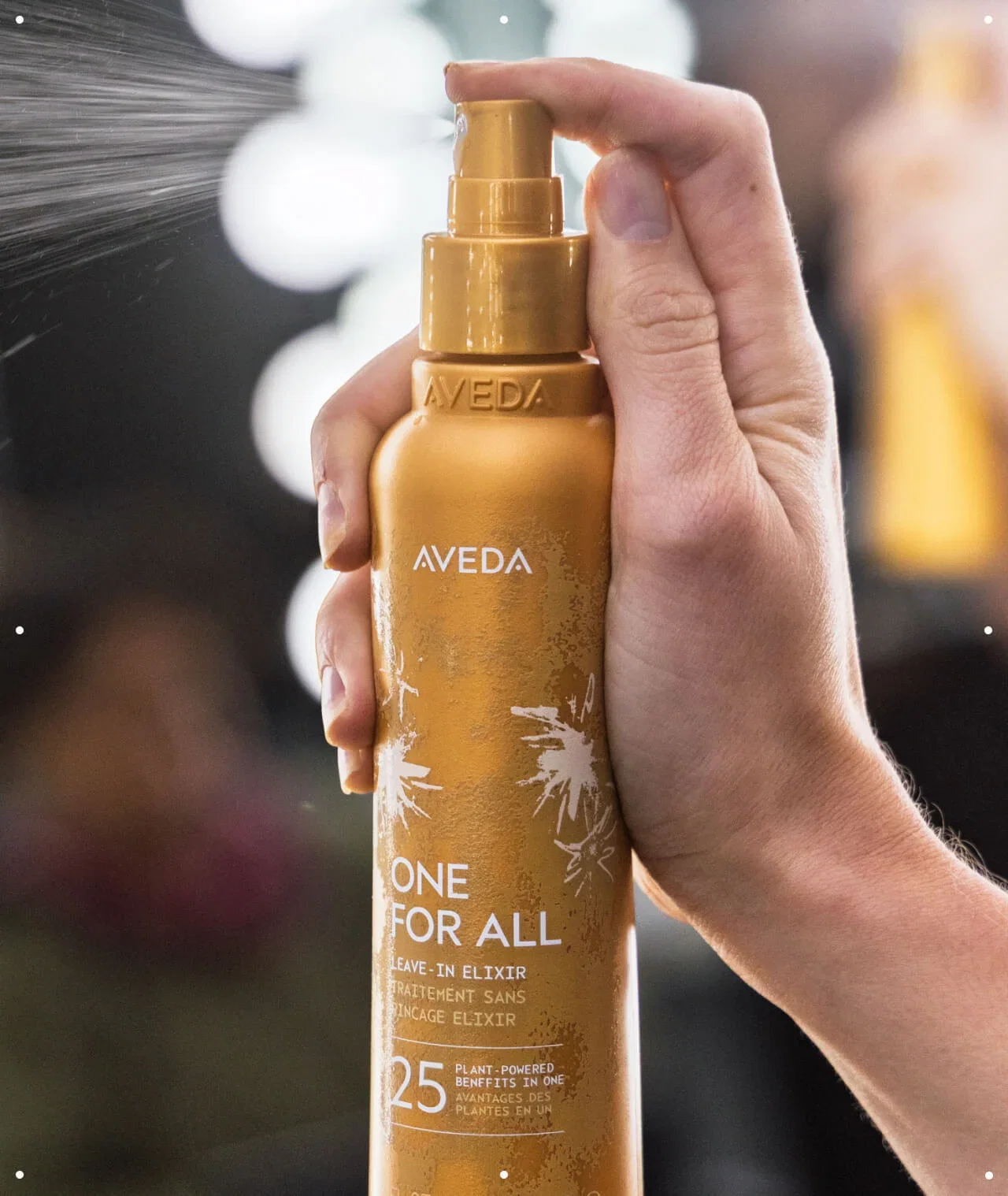 Close-up of a hand spraying Aveda One For All Leave-In Elixir.