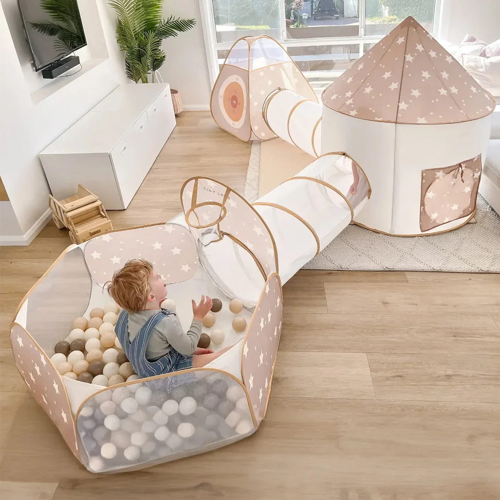 Child playing in connected play tent and tunnel system with ball pit, in neutral beige and white with star patterns