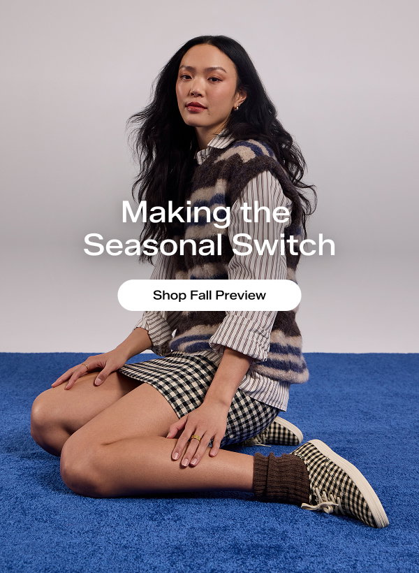 A woman sitting on blue rug. She is wearing a striped button-up, soft, striped sweater vest, a check-print mini skirt, brown socks, and the Keds Champion Buffalo Plaid Lace-Up in black/parchment, a color that matches the skirt. The email says Making the Seasonal Switch. Shop Fall Preview.