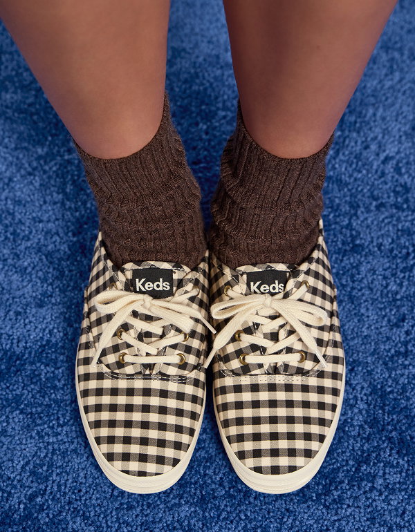 An overhead view of a woman standing on a blue carpet wearing the Keds Champion Buffalo Plaid Lace-Up in black/parchment paired with brown socks.