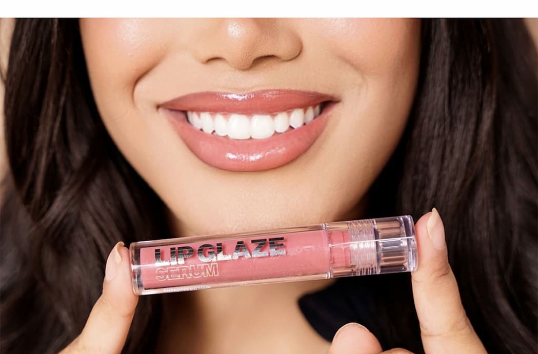 Model wearing a glossy nude-pink lip and holding Palladio Lip Glaze Serum.