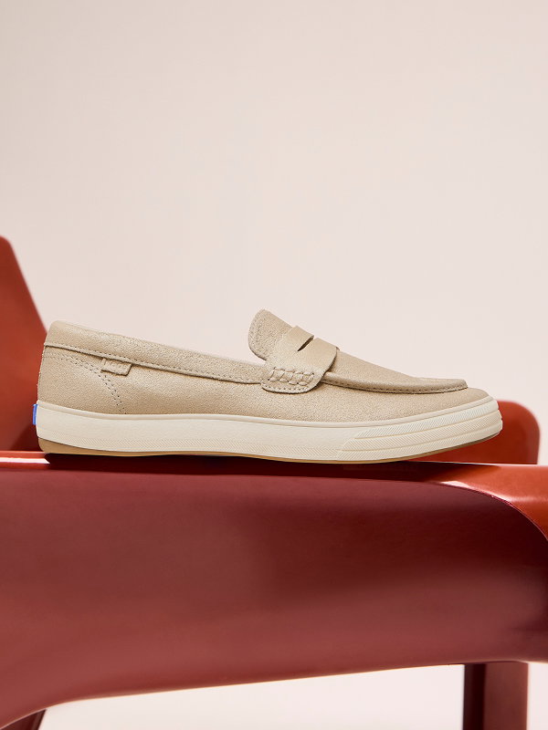 A side view of the Center III Metallic Suede Loafer in champagne positioned on a brown armchair. 