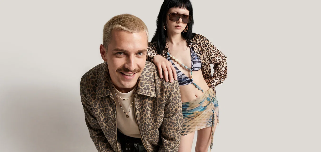 Un hombre y una mujer con conjuntos coordinados de estampado de leopardo posan con confianza frente a un fondo liso.
