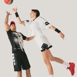 Dos jugadores de baloncesto en el aire alcanzando el balón, vestidos con ropa deportiva negra y blanca sobre un fondo liso.
