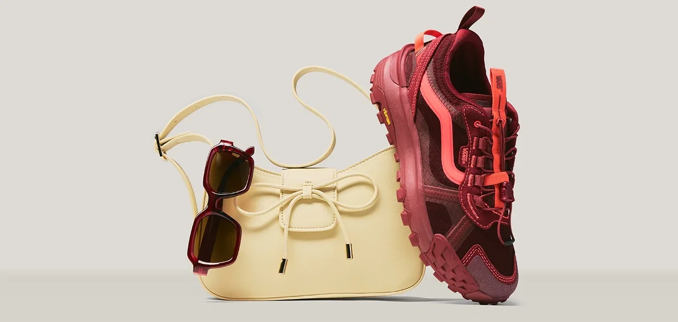 Bolso beige con detalle de lazo, gafas de sol oscuras colgadas de la correa y una zapatilla deportiva roja y rosa apoyada en el bolso.