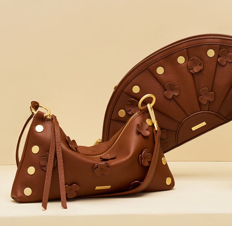 Studio image featuring the Hammitt Kyle Med in Sienna Flora alongside the coordinating Olympia Clutch, highlighting rich brown pebbled leather, sculpted leather floral appliqués, signature rivets, and brushed gold hardware.