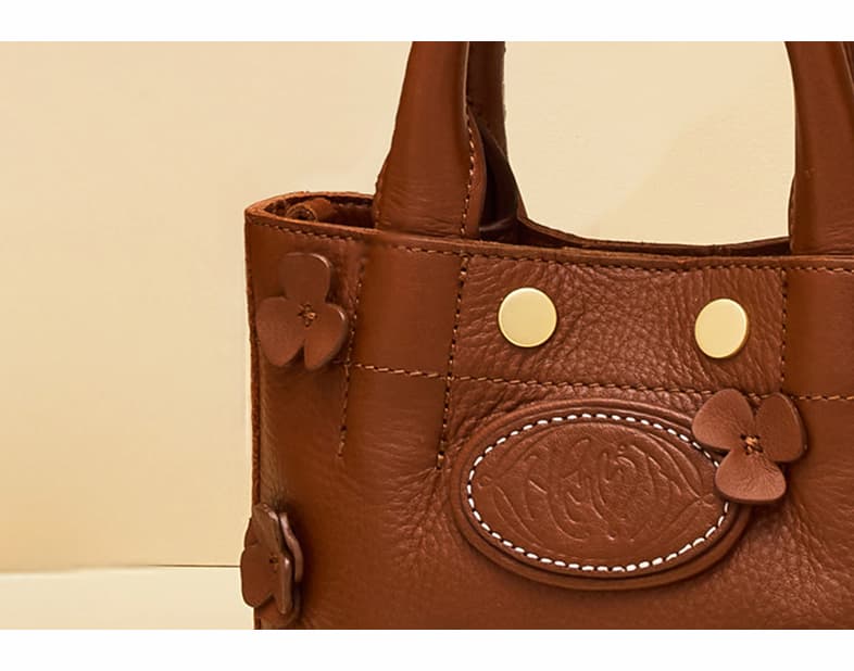 Close-up of the Hammitt Olympia Crossbody Sml in Sienna Flora, showcasing rich brown pebbled leather, embossed Hammitt logo, brushed gold hardware, and handcrafted leather floral appliqués.