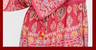 Ein Model trägt eine rot-gemusterte Longbluse mit Trompetenärmeln