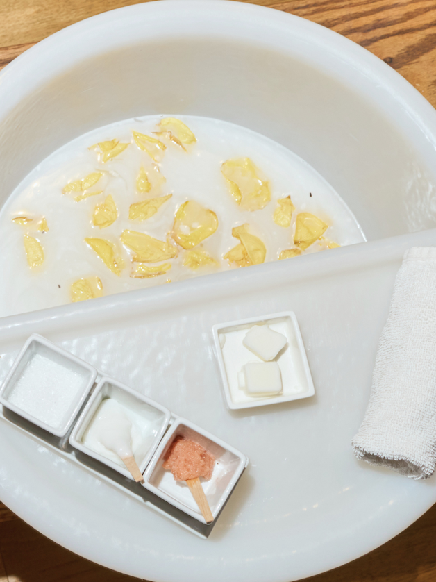 Foot soak with flower petals, scrub, lotion, and a towel prepared for a spa pedicure.