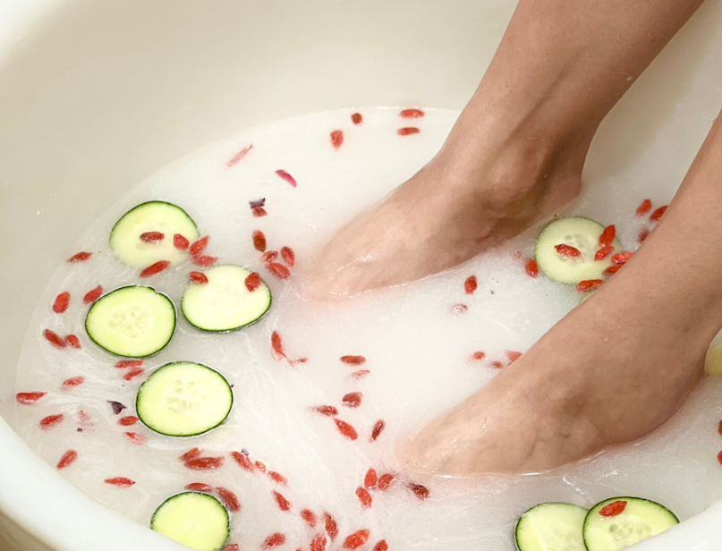 Feet soaking in a creamy coconut milk bath with cucumber slices and goji berries.