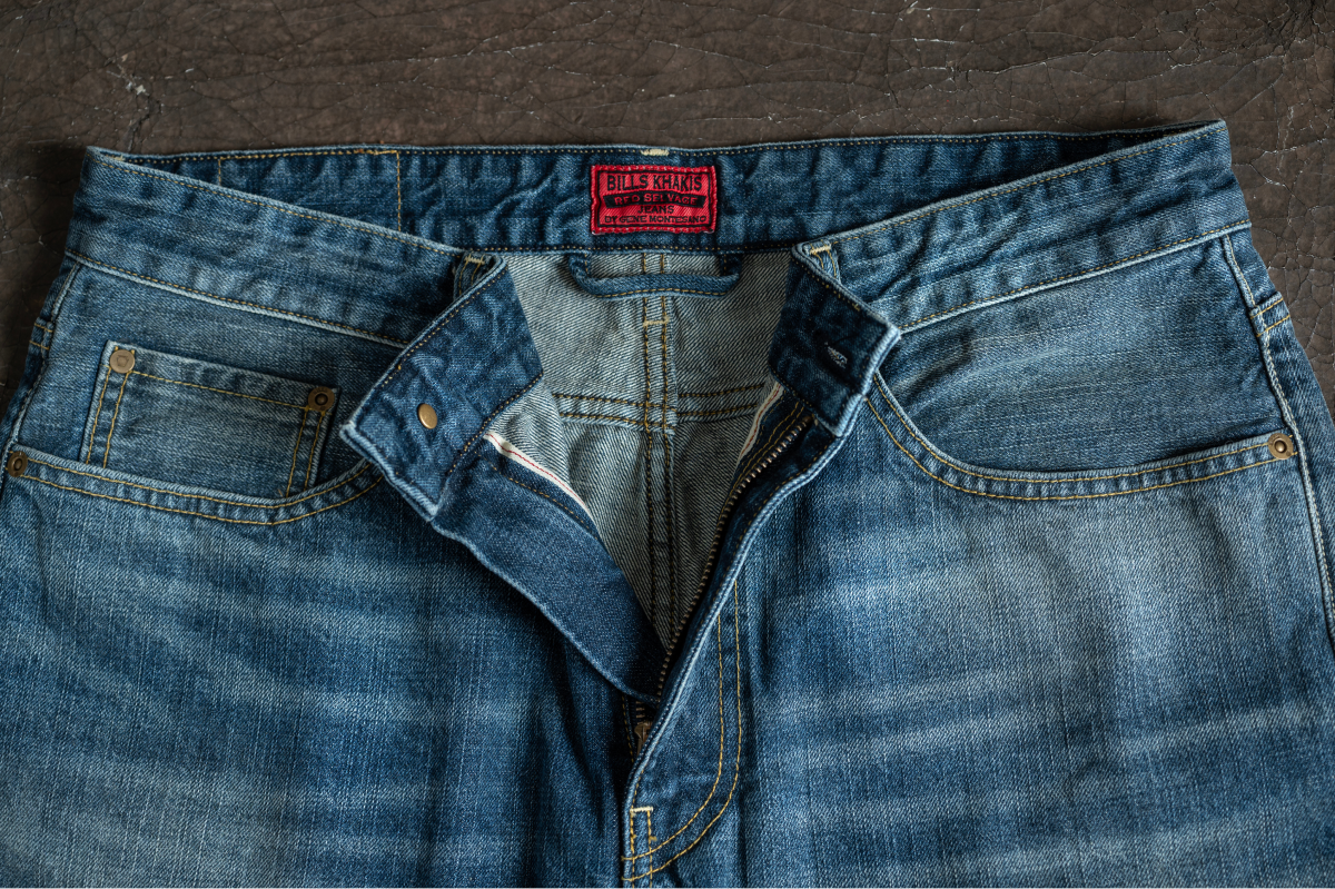 A pair of Bills Khakis Rede Selvedge denim by Gene Montesano its on display on a indstrial brown backdrop