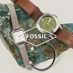 Deux montres-bracelets — une argentée avec un bracelet en maille, une avec un cadran vert et un bracelet en cuir marron — et un bracelet noir sur une pierre verte rugueuse.