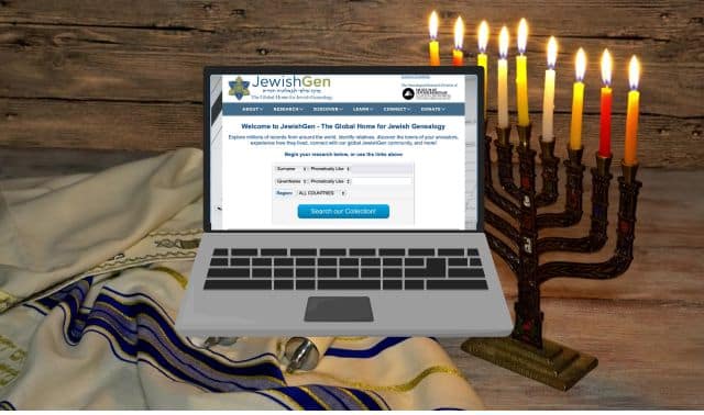 A laptop displaying a genealogy website sits on a table next to a menorah with lit candles and a folded tallit.