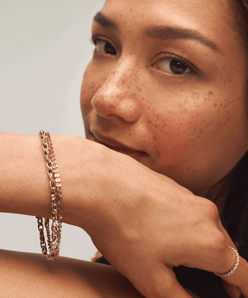 Woman wearing layered yellow gold chain bracelets and a diamond band ring.
