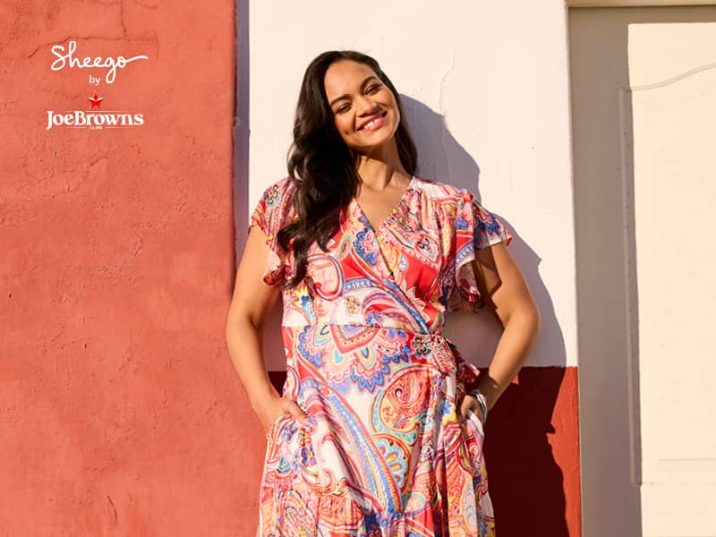 Ein Model trägt ein ecru-rot-gemustertes Chiffonkleid in Wickeloptik mit Allover-Paisleydruck, V-Ausschnitt und Flügelärmeln. Daneben ist das Sheego by Joe Browns Logo abgebildet.